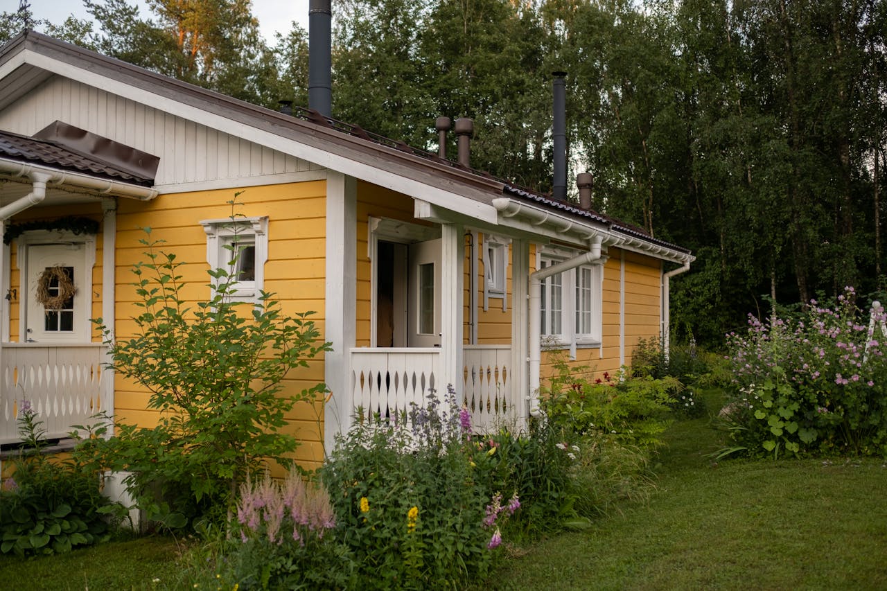 A picturesque yellow cottage surrounded by lush greenery and summer blooms in a peaceful rural area.
