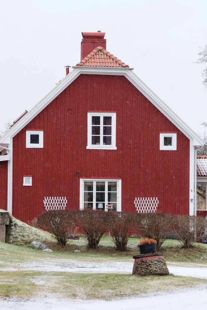 gallery-2 A picturesque red wooden house with a snowy yard in a rural winter setting.