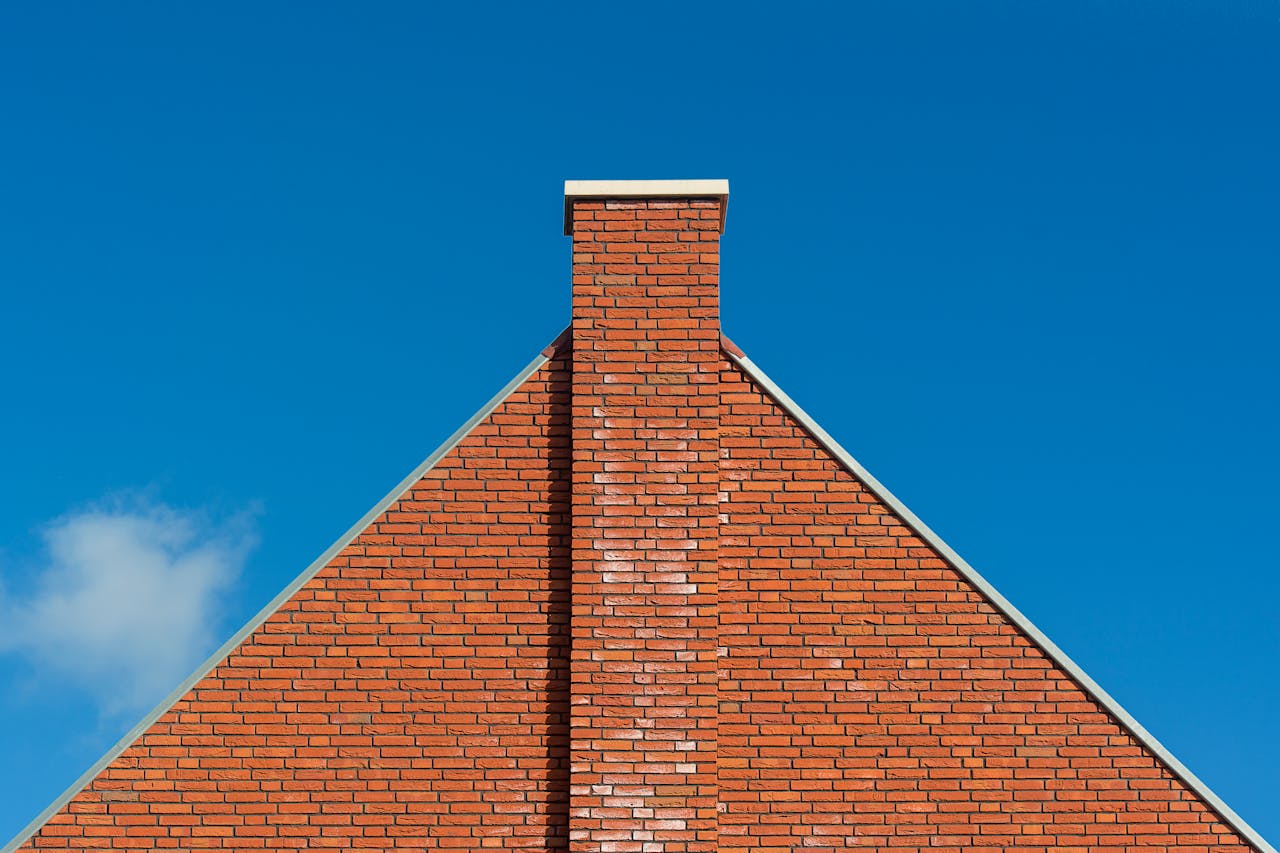 our-services-3 Red brick wall with chimney against clear blue sky, emphasizing architectural design.