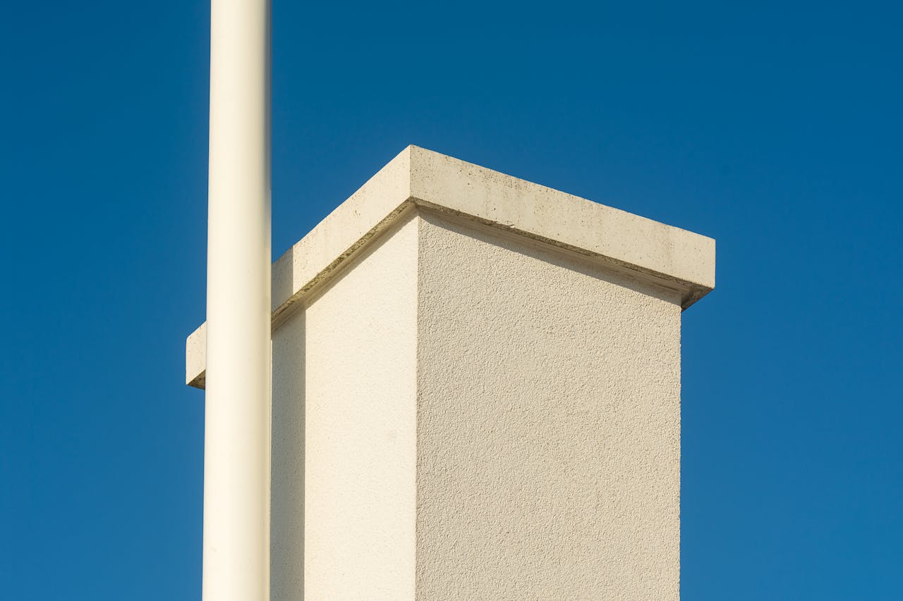 gallery-5 Minimalist architecture featuring a white column and chimney under a blue sky, perfect for design inspiration.