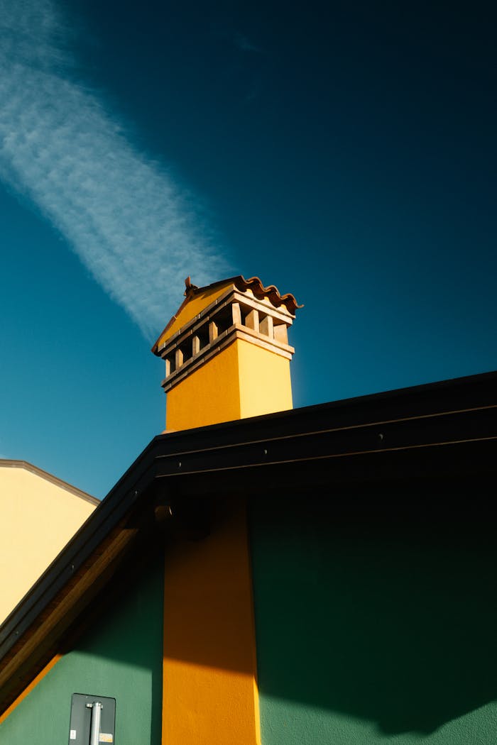 gallery-6 Vibrant yellow and green building rooftop with chimney against a clear blue sky, showcasing colorful architecture.
